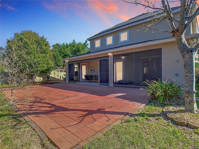 back of house at dusk with a patio, a sunroom, and stucco siding