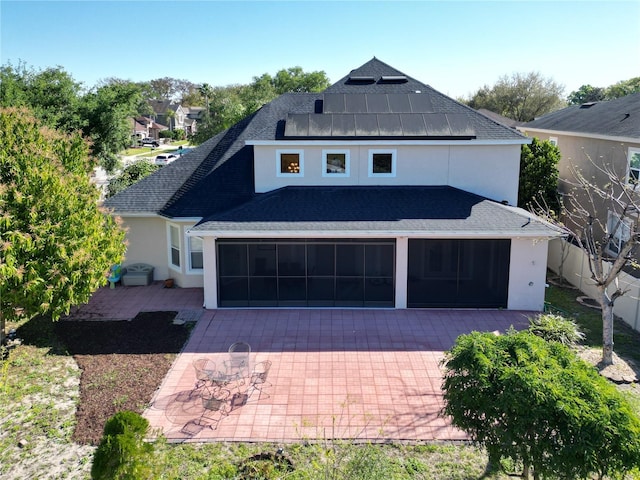 view of front facade featuring stucco siding, a patio, a shingled roof, a sunroom, and solar panels