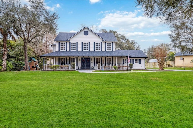 country-style home featuring roof with shingles, covered porch, a front yard, and fence