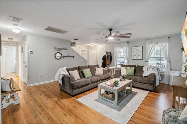 living room with visible vents, baseboards, light wood-style floors, and a textured ceiling