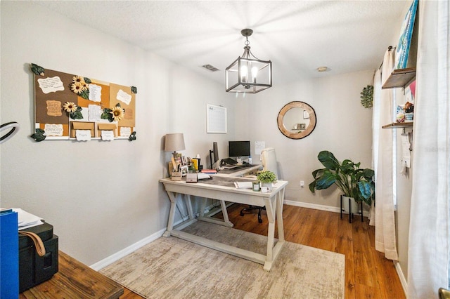 office featuring wood finished floors, visible vents, a chandelier, and baseboards