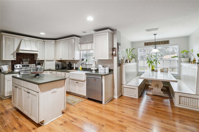 kitchen with premium range hood, a sink, dark countertops, light wood-style floors, and appliances with stainless steel finishes