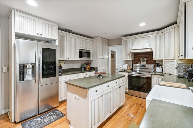 kitchen featuring dark countertops, a kitchen island, premium range hood, appliances with stainless steel finishes, and light wood-style floors