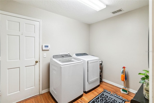 laundry area featuring washing machine and clothes dryer, visible vents, baseboards, light wood-type flooring, and laundry area