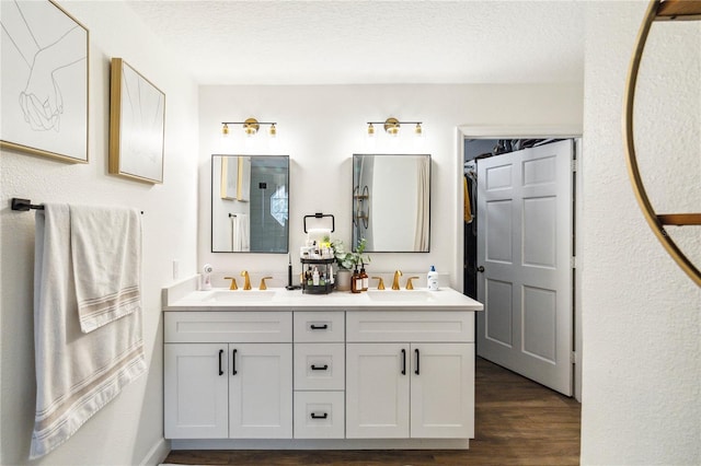 full bathroom featuring double vanity, a textured ceiling, wood finished floors, and a sink