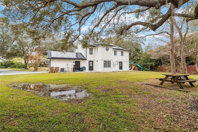 back of property with solar panels, a playground, a yard, and fence