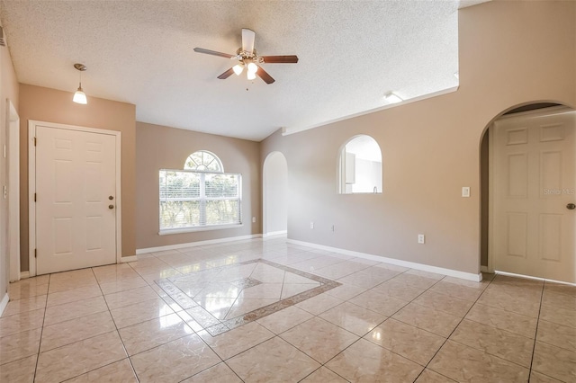 empty room featuring light tile patterned floors, baseboards, arched walkways, and a textured ceiling