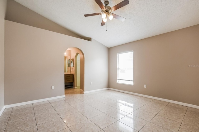 spare room featuring vaulted ceiling, light tile patterned flooring, arched walkways, and a textured ceiling