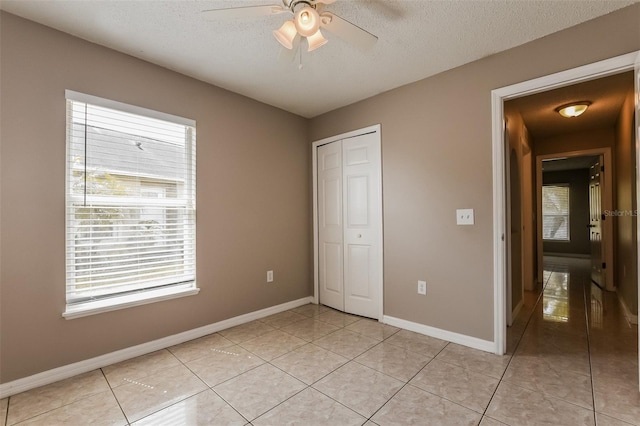 unfurnished bedroom featuring light tile patterned floors, baseboards, a closet, and a textured ceiling