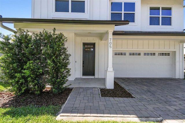 doorway to property featuring board and batten siding, an attached garage, and decorative driveway