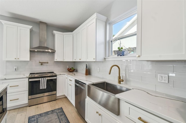 kitchen featuring appliances with stainless steel finishes, white cabinetry, wall chimney exhaust hood, and a sink