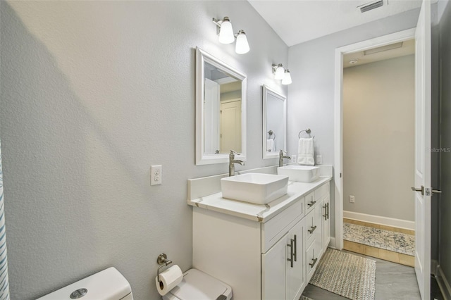 bathroom with double vanity, toilet, visible vents, and a sink