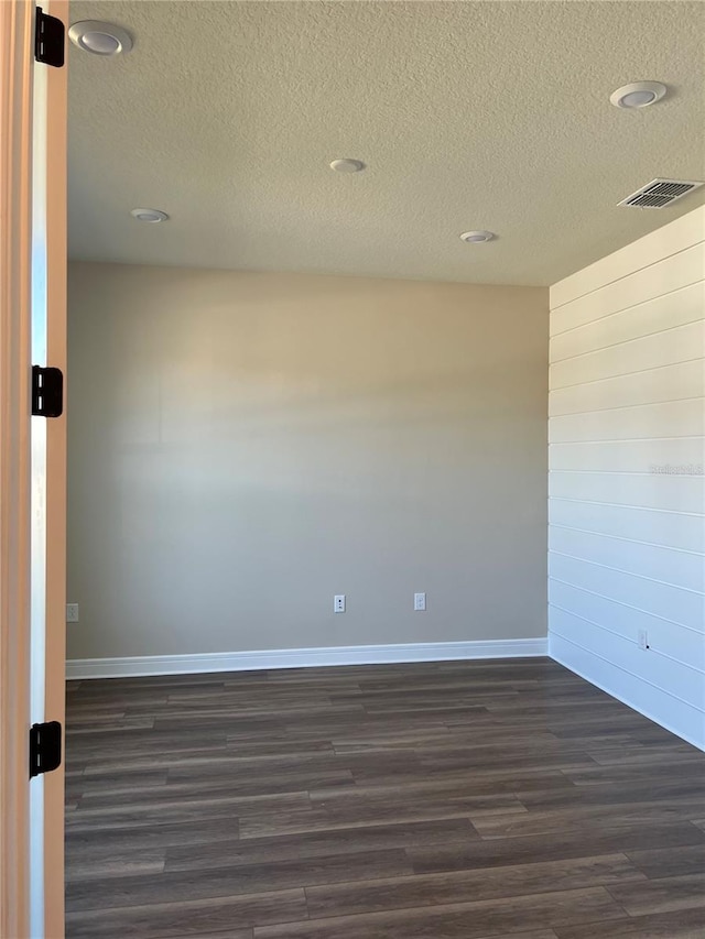 unfurnished room featuring visible vents, a textured ceiling, dark wood-type flooring, and baseboards