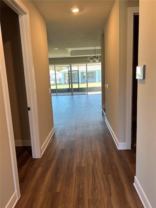 corridor with dark wood finished floors, a textured ceiling, and baseboards