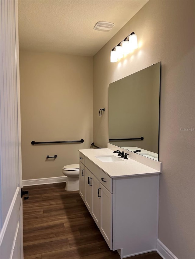 half bath with baseboards, toilet, vanity, wood finished floors, and a textured ceiling