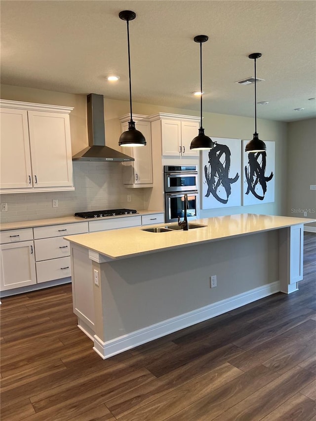 kitchen featuring a sink, gas cooktop, double oven, wall chimney exhaust hood, and dark wood-style flooring