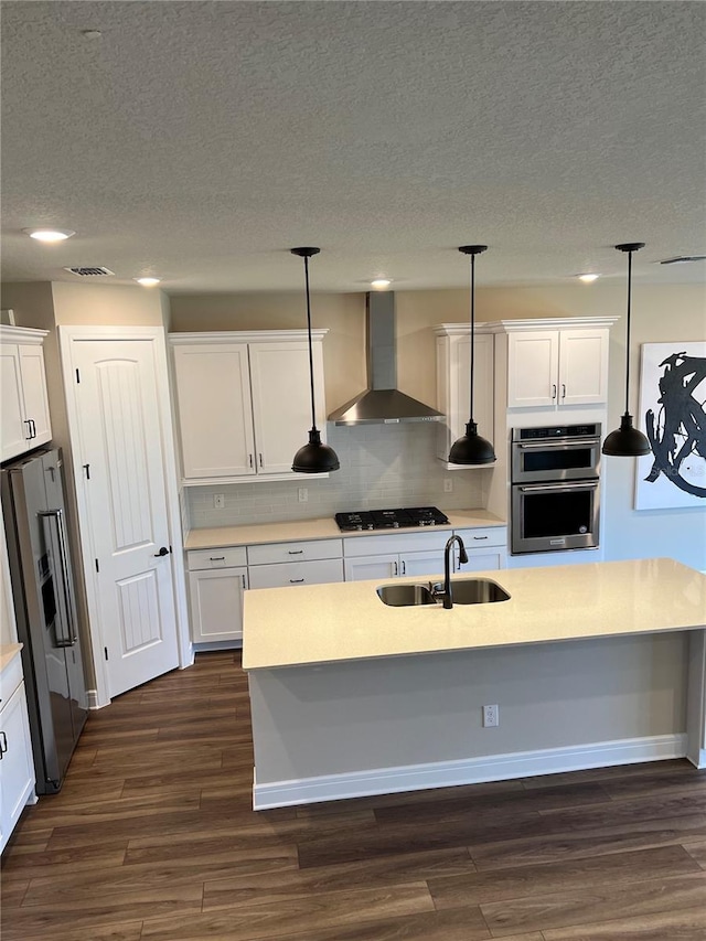 kitchen with dark wood-style floors, a sink, appliances with stainless steel finishes, white cabinetry, and wall chimney range hood