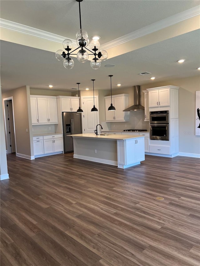 kitchen featuring ornamental molding, appliances with stainless steel finishes, white cabinets, wall chimney exhaust hood, and a kitchen island with sink