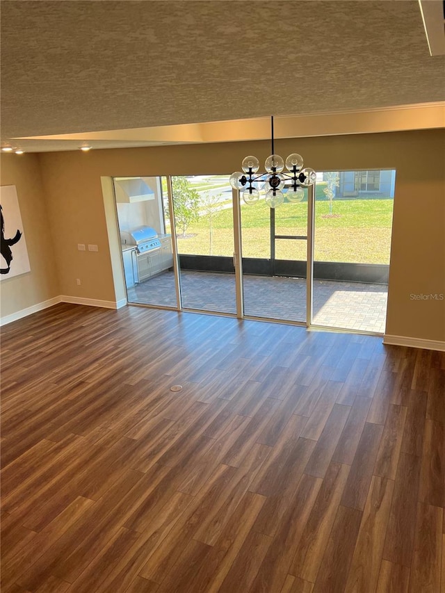 spare room with an inviting chandelier, dark wood-type flooring, and baseboards