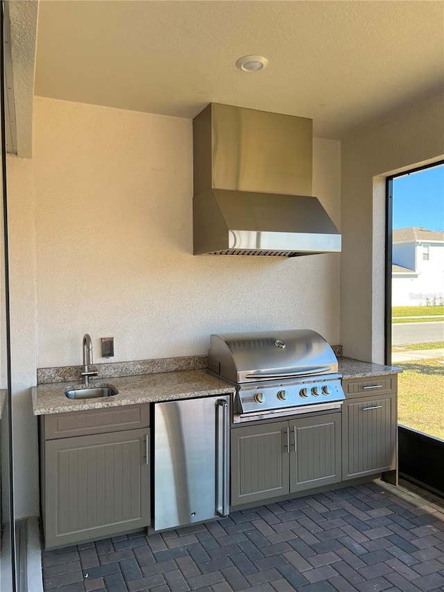 kitchen with a sink, gray cabinetry, wall chimney exhaust hood, and freestanding refrigerator