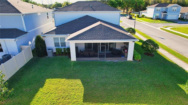 rear view of house with fence, roof with shingles, a yard, a sunroom, and a residential view