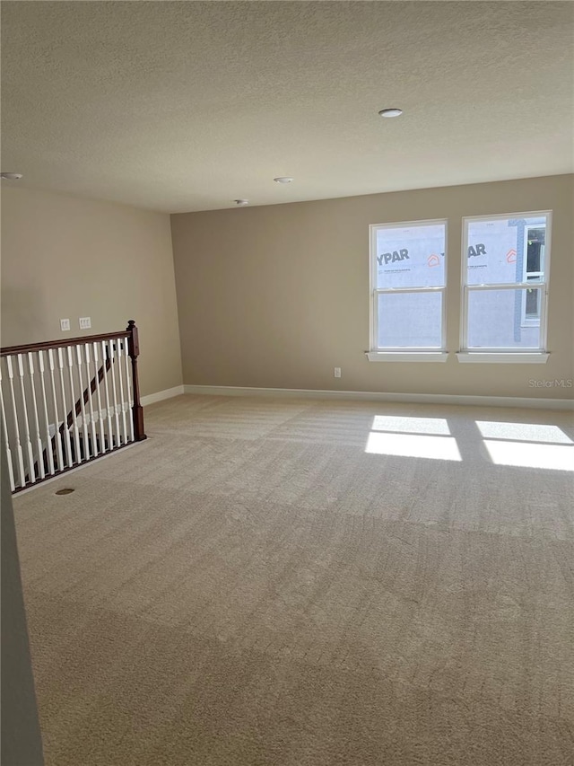 spare room with light colored carpet, baseboards, and a textured ceiling