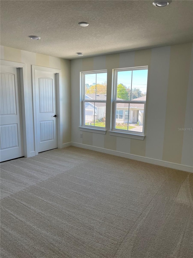 unfurnished room with light colored carpet, baseboards, and a textured ceiling