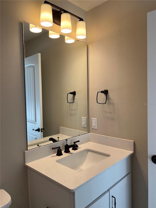 bathroom with toilet, vanity, and a textured wall