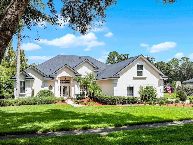 view of front of property with stucco siding, roof with shingles, and a front yard