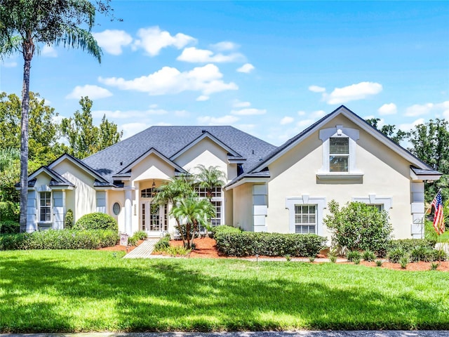 view of front of house featuring stucco siding, a shingled roof, and a front lawn