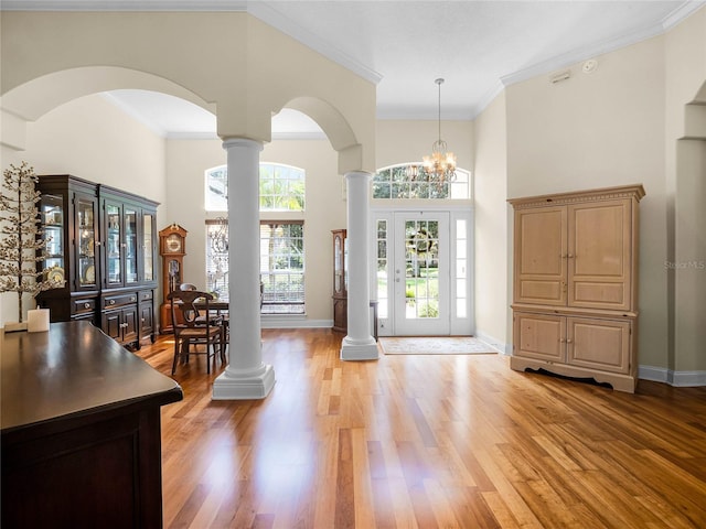 foyer entrance featuring baseboards, a high ceiling, decorative columns, arched walkways, and light wood-style floors