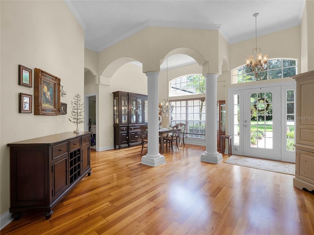 foyer entrance with a notable chandelier, a high ceiling, light wood-style floors, and decorative columns