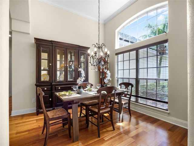 dining area featuring light wood-type flooring, ornamental molding, a high ceiling, an inviting chandelier, and baseboards