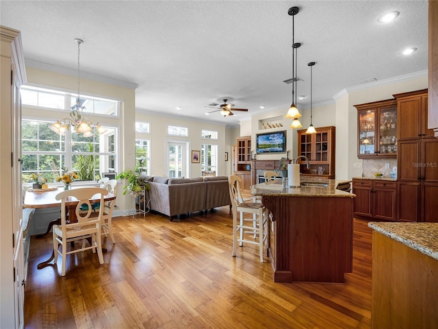 kitchen with a breakfast bar area, brown cabinets, wood finished floors, and ceiling fan with notable chandelier