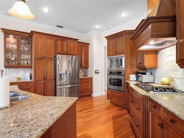 kitchen with visible vents, light wood-style flooring, custom range hood, stainless steel appliances, and brown cabinetry