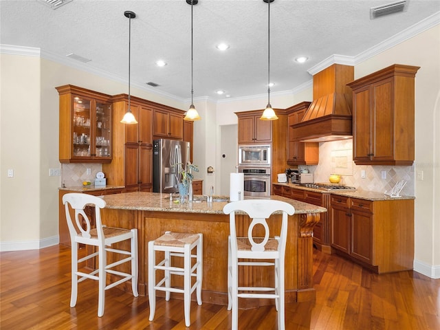 kitchen featuring visible vents, brown cabinets, a sink, stainless steel appliances, and custom exhaust hood