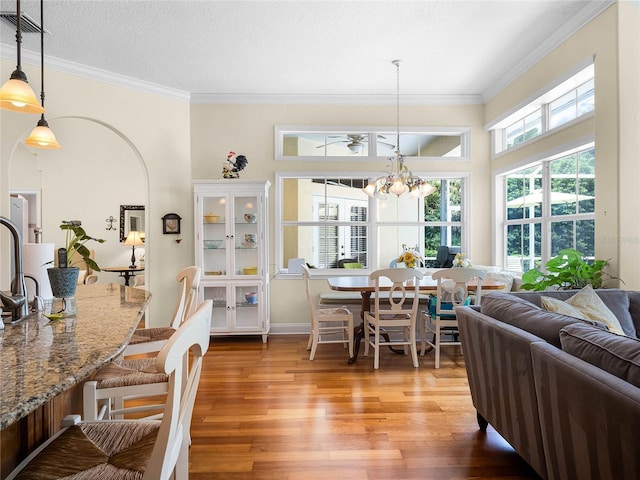 dining space featuring a notable chandelier, crown molding, a textured ceiling, and light wood-type flooring