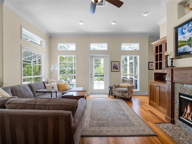 living area with ceiling fan, light wood-style flooring, a fireplace, and crown molding