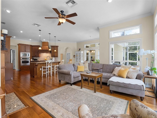 living room with visible vents, wood finished floors, crown molding, and ceiling fan with notable chandelier