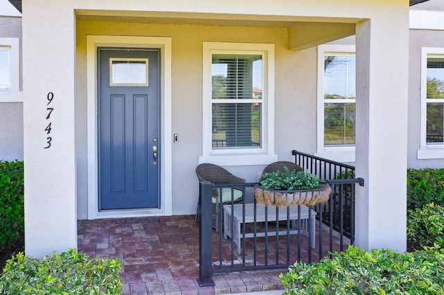 view of exterior entry with stucco siding and a porch