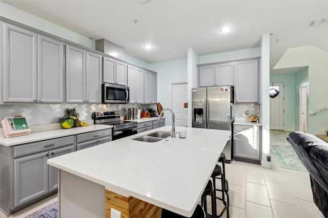 kitchen featuring a breakfast bar, gray cabinetry, a sink, appliances with stainless steel finishes, and light countertops