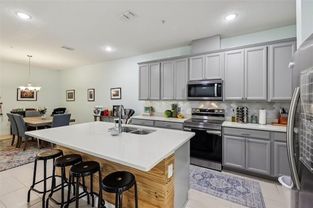 kitchen featuring visible vents, a breakfast bar, gray cabinetry, a sink, and appliances with stainless steel finishes