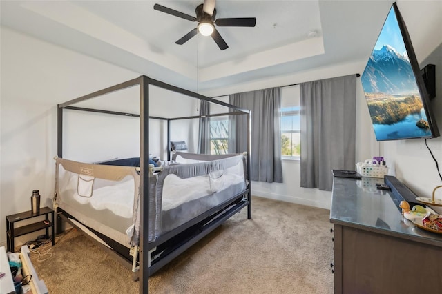 bedroom with a tray ceiling, baseboards, light colored carpet, and ceiling fan