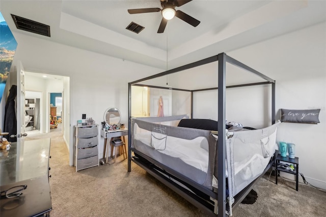 bedroom with a raised ceiling, a ceiling fan, visible vents, and carpet floors