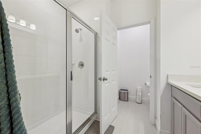 bathroom with vanity, a shower stall, toilet, and baseboards