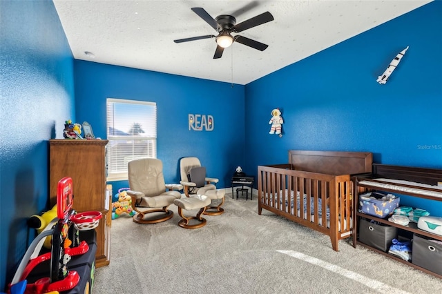 carpeted bedroom featuring a crib, ceiling fan, and a textured ceiling