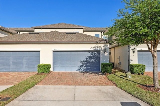 view of front of home featuring stucco siding, a shingled roof, and decorative driveway