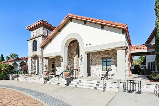 mediterranean / spanish-style home featuring stucco siding, stone siding, a porch, and a tile roof