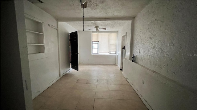 corridor featuring built in shelves, a textured wall, and a textured ceiling