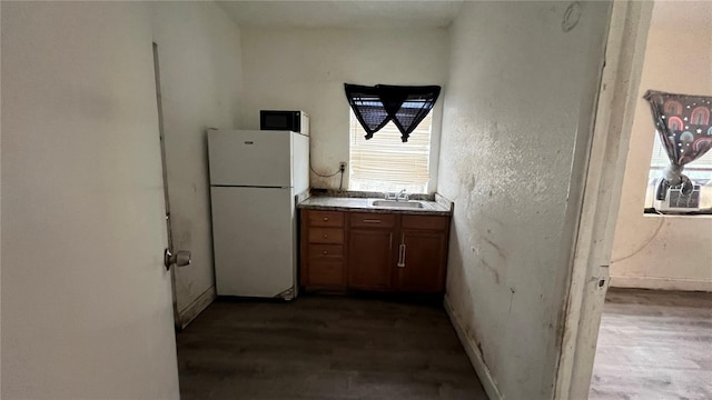 kitchen featuring brown cabinetry, wood finished floors, freestanding refrigerator, and a sink